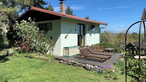 Una casa pequeña con terraza, un escoba y mobiliario exterior.