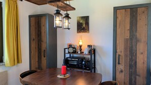 A dining area with a wooden table, two chairs, a red candle, a radio, a lamp, and a painting on the wall.