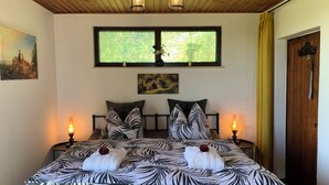 A bedroom with a bed, two bedside tables, a window, a door, and artwork on the walls.