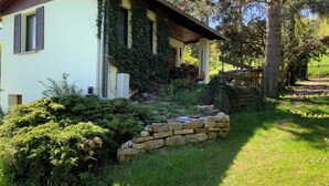 A house with a stone retaining wall, a wooden deck, and a garden with various plants and a stone pathway.
