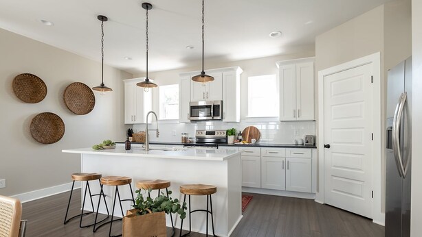 Une cuisine moderne avec des meubles blancs, un îlot central doté de tabourets, des luminaires suspendus et un réfrigérateur en acier inoxydable.