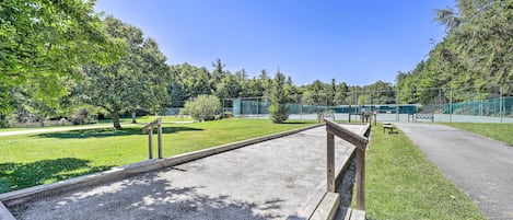 A gravel area with wooden railings, surrounded by green grass and trees, with a fence in the background.
