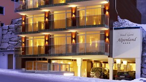 Un hotel de varios pisos con balcones, ventanas amplias y un letrero que indica que es el Hotel Garni Alpenland.
