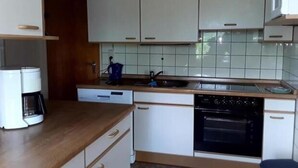 Una cucina compatta con mobili bianchi, forno integrato, macchina da caffè e lavello.