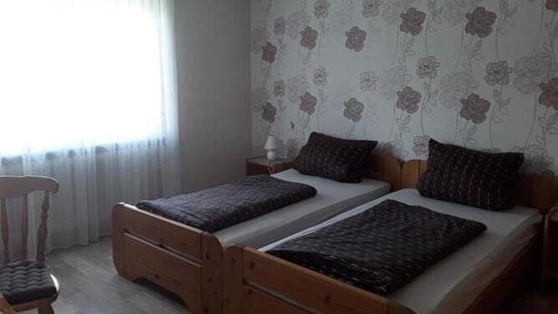 Una stanza con due letti in legno, una sedia, un comodino e una finestra con tende.