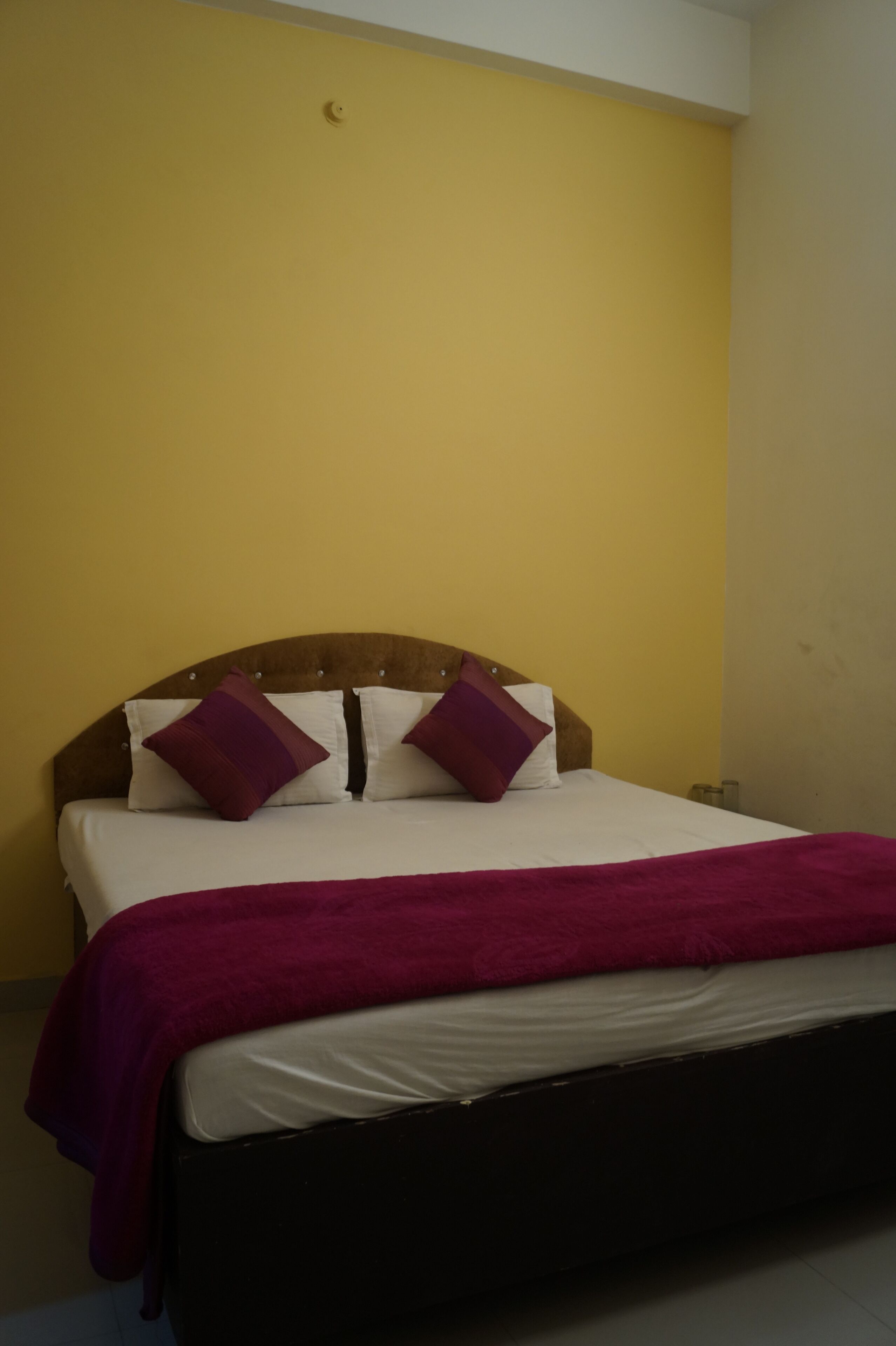 Ein Bett mit hölzernem Kopfteil, zwei weiße Kissen und einer violetten Tagesdecke.