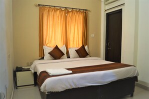 A hotel room with a bed, a nightstand, a telephone, and a door. - Hotel Sunrise Inn (Kota)