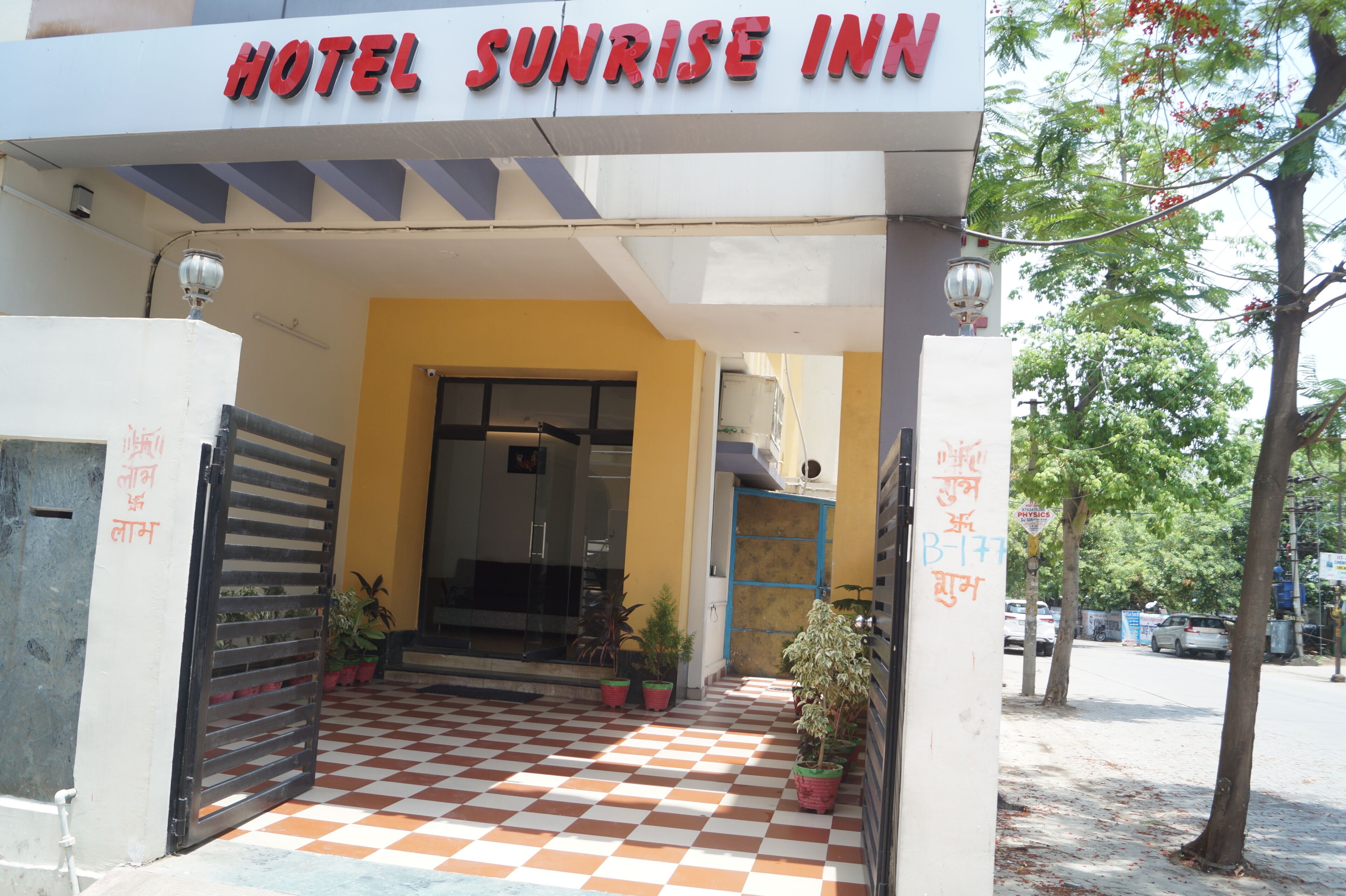 The entrance to Hotel Sunrise Inn with a checkered floor pattern, potted plants, and a signboard.