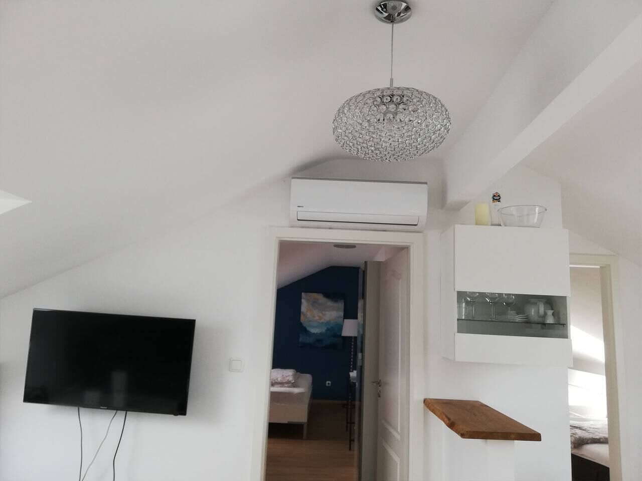 A modern living room with a flat-screen TV, a decorative crystal chandelier, and a built-in air conditioning unit.