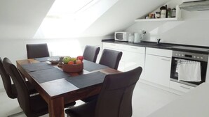 Una cocina moderna con comedor, que incluye una mesa de madera, sillas, un tazón de fruta y un horno empotrado.