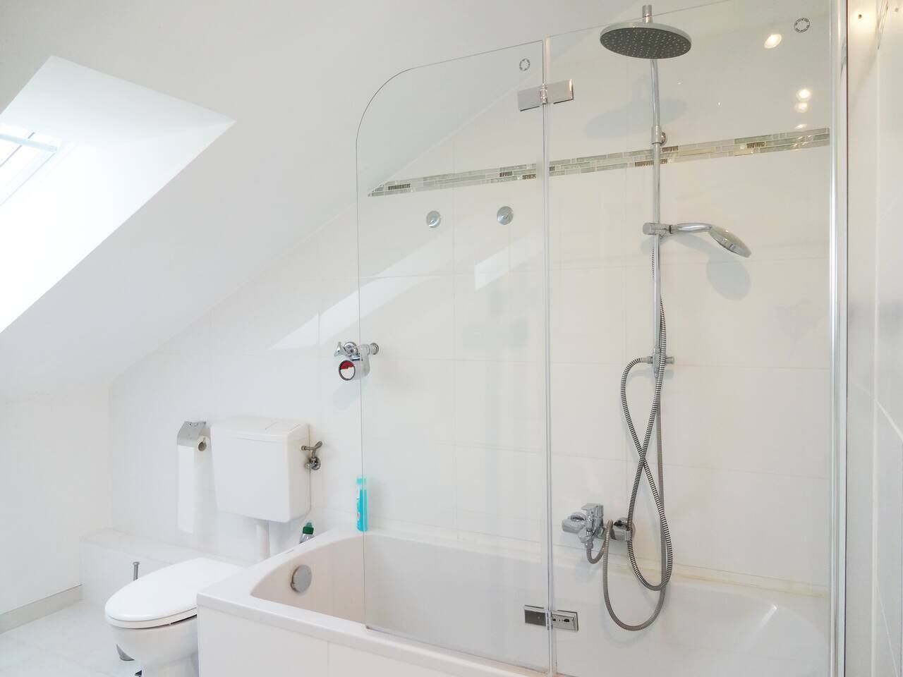 Een moderne badkamer met een douchecabine van glas, een witte badkuip en een toilet.