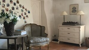 A room with a vintage armchair, a small table with a vase of flowers, a dresser with lamps, and a wall adorned with photos. - Charming house on the Ile de Ré (Loix)