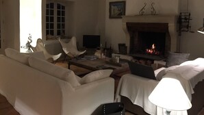 A living room with a fireplace, white furniture, and a television. - Charming house on the Ile de Ré (Loix)