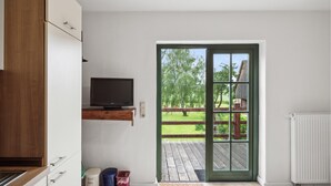 A modern kitchen with a built-in TV, a wooden cabinet, and a view of a wooden deck and trees outside. - Nice apartment in Am Salzhaff with WiFi (Am Salzhaff)