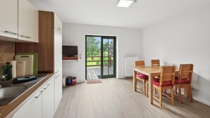 A modern kitchen with wooden cabinets, a built-in TV, and a dining area with wooden chairs and a table. - Nice apartment in Am Salzhaff with WiFi (Am Salzhaff)