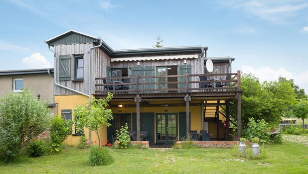 A two-story building with a balcony, a covered porch, and a garden area. - Nice apartment in Am Salzhaff with WiFi (Am Salzhaff)