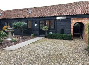 Traditional building with a brick archway entrance, set amidst a garden with a gravel driveway and shrubs.