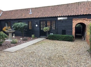 Traditional building with a brick archway entrance, set amidst a garden with a gravel driveway and shrubs.