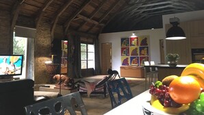 Ein rustikaler Innenraum mit Gewölbedecke, einem Fernseher, einer Essecke mit Obst und Kunstwerken an den Wänden.