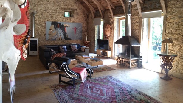 Ein rustikales Interieur mit einer Steinwand, Holzbalken an der Decke, einem Kamin, einer Couch, einem Fernseher und einem großen Gemälde.