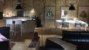 Ein rustikales Interieur mit freiliegenden Holzbalken, einer Küche mit modernen Geräten, einem Essbereich mit Tisch und Stühlen sowie Kunstwerken an den Wänden.