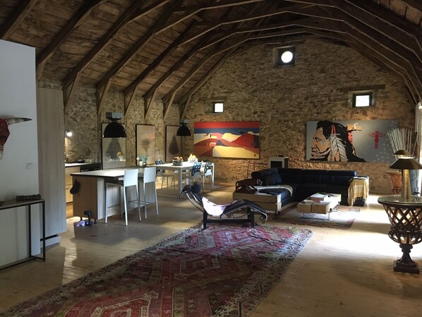 Un interior rústico con pared de piedra, zona de comedor, sofá y alfombra estampada.