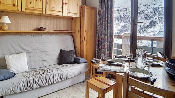 A cozy room with a sofa, wooden cabinets, a dining table with chairs, and a window with a view of a snowy landscape. - Functional studio in Menuires, close to slopes, balcony (Les Menuires)