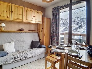 A cozy room with a sofa, wooden cabinets, a dining table with chairs, and a window with a view of a snowy landscape. - Functional studio in Menuires, close to slopes, balcony (Les Menuires)