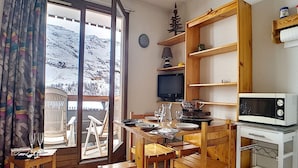 A cozy room with a wooden table, chairs, a TV, and a view of a snowy mountain. - Functional studio in Menuires, close to slopes, balcony (Les Menuires)