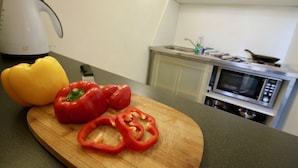 Une cuisine avec une planche à découper sur laquelle se trouvent des poivrons rouges, une bouilloire et un four à micro-ondes.