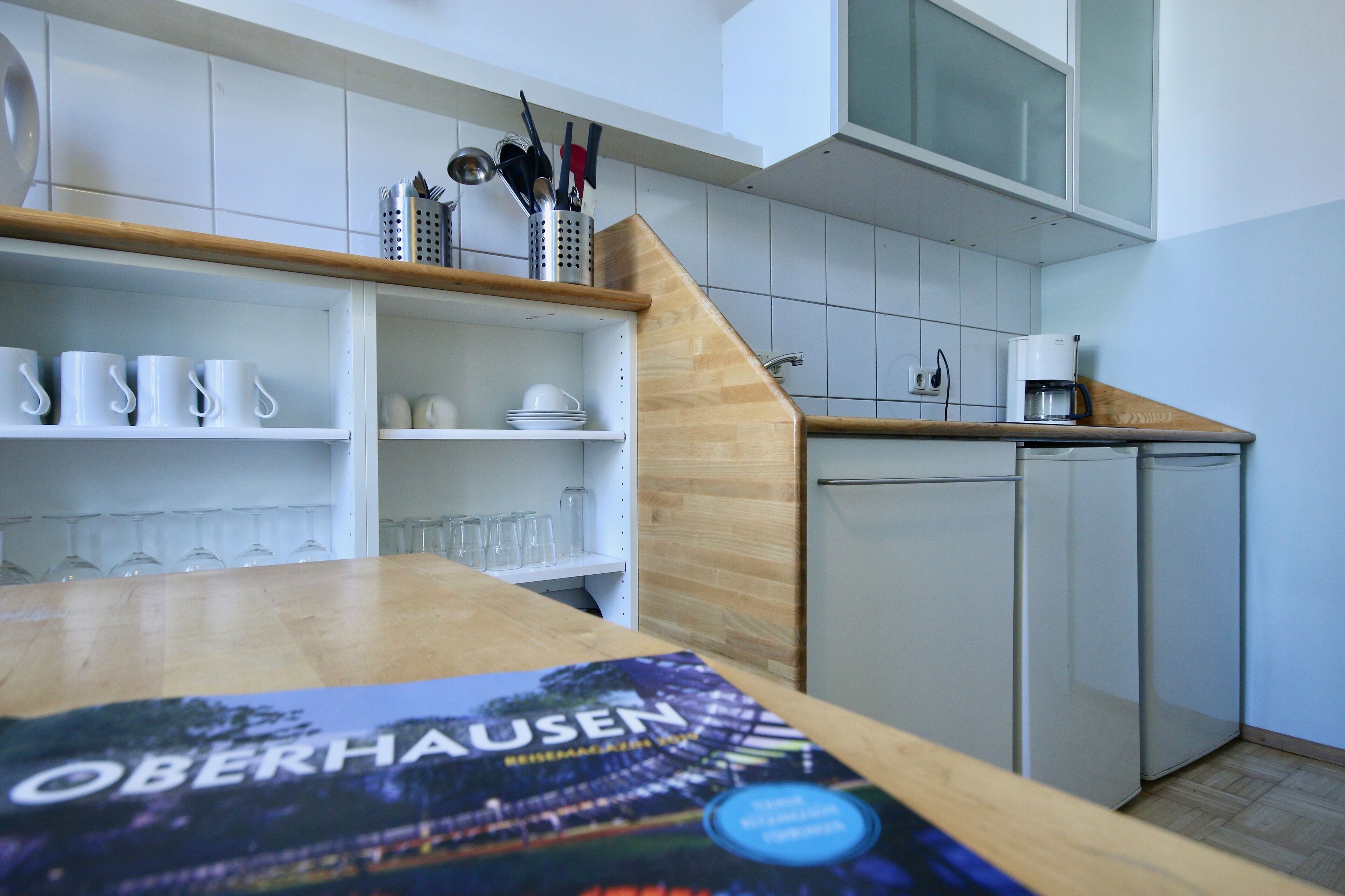 A modern kitchen with white cabinets, a wooden countertop, and a coffee machine.