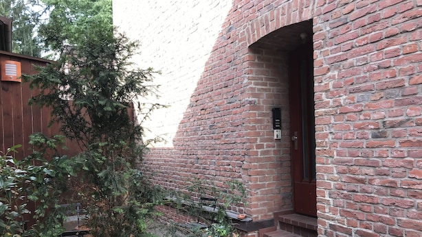 Un bâtiment en briques avec une porte en bois et des marches menant à un porche.