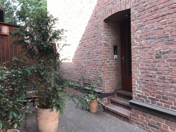 Step into a serene courtyard surrounded by lush greenery and a historic brick building.
