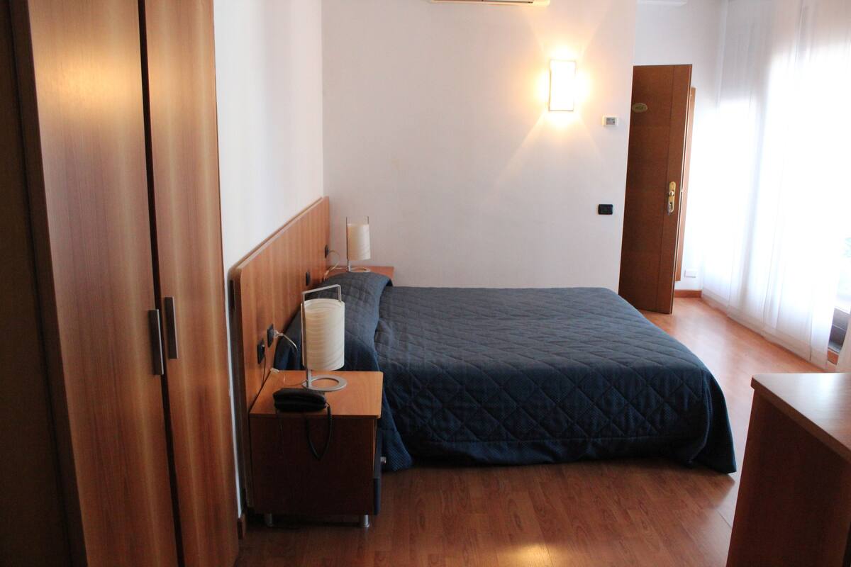 A bedroom with a bed, bedside table, lamp, and wooden wardrobe.