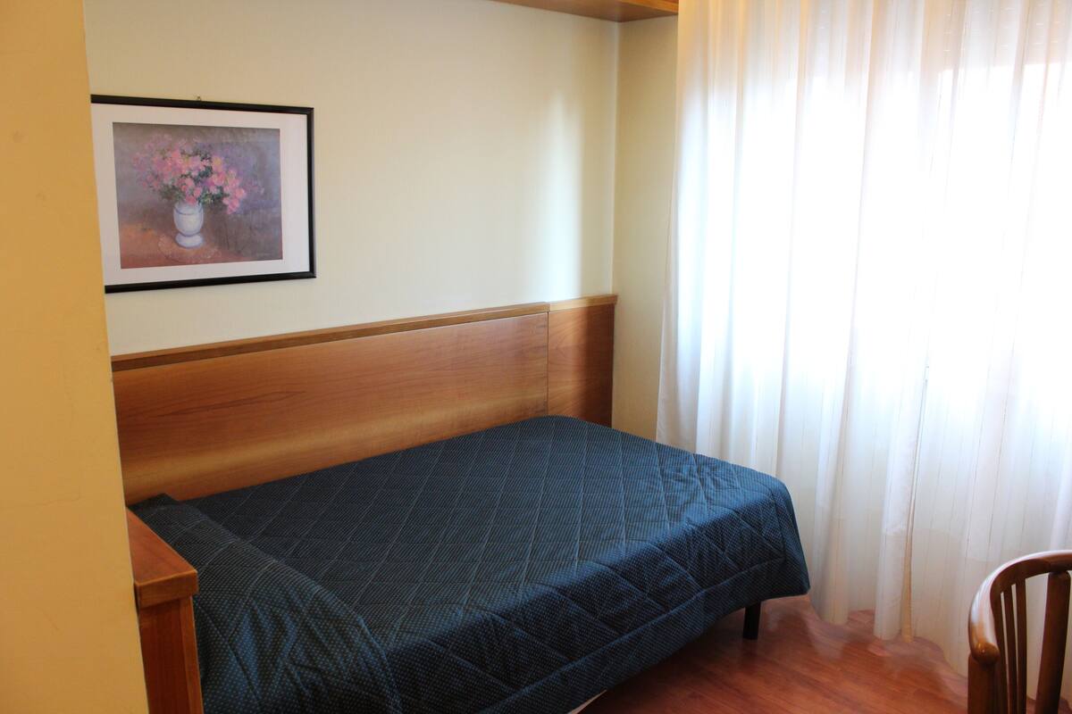 A single bed with a wooden headboard in a room with a plain wall and a framed painting.