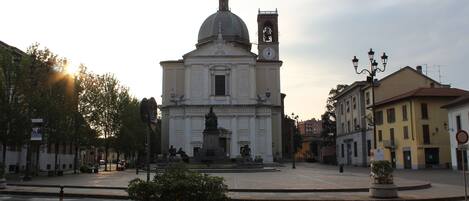 Un edificio histórico con cúpula y torre del reloj, rodeado de una plaza adoquinada con bancos y plantas en macetas.