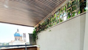 Terraço no telhado com telhas de barro, teto de madeira e vista para uma igreja com cúpula e torre do relógio.