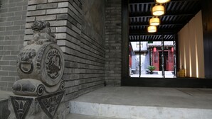 A stone lion statue at the entrance of a building with a traditional tiled roof and hanging lanterns. - True Go Hotel (Beijing)
