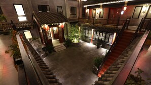 A traditional courtyard with a wooden staircase, potted plants, and a small garden area. - True Go Hotel (Beijing)