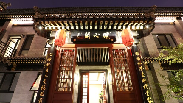 A traditional Chinese building entrance with a tiled roof, wooden doors, and illuminated signs. - True Go Hotel (Beijing)