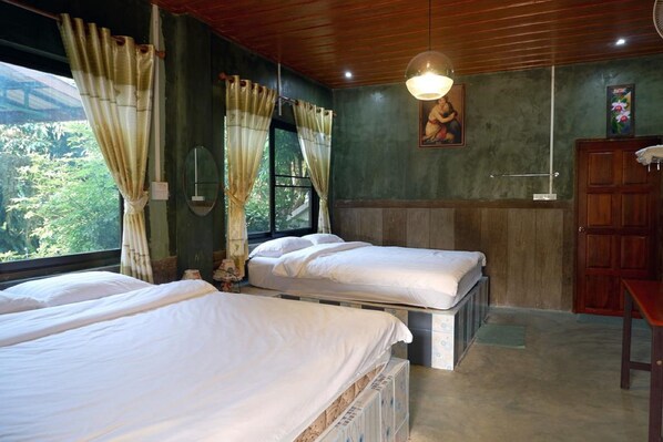 A room with two beds, a wooden ceiling, a window with curtains, a painting on the wall, and a wooden cabinet.
