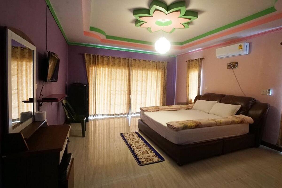Quarto com cama, escrivaninha, cadeira, televisão e ventoinha no teto.