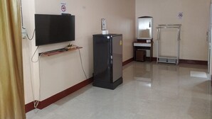 A hotel room with a flat-screen TV mounted on the wall, a refrigerator, a small table with a mirror, and a metal stand. - Rattikanchana Resort (Mae Fa Luang)