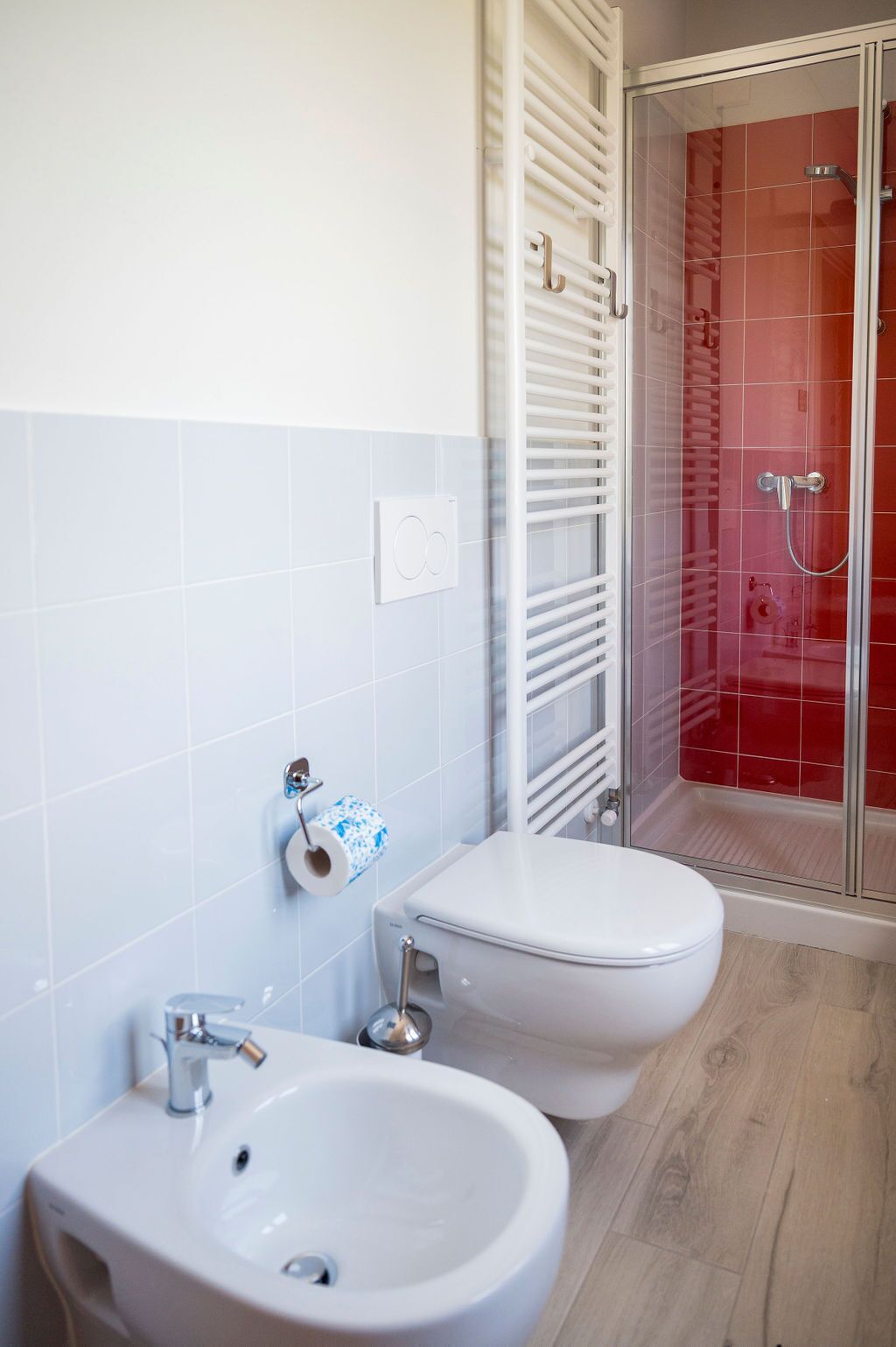 A bathroom with two toilets, a sink, and a shower with red tiles.