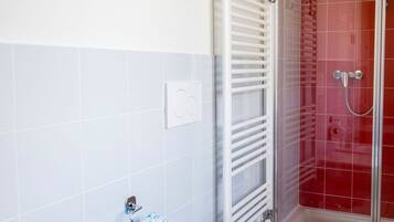 A bathroom with two toilets, a sink, and a shower with red tiles.