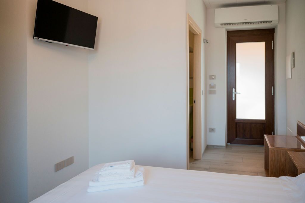 A hotel room with a bed, a TV mounted on the wall, a wooden desk, and a door leading to another room.