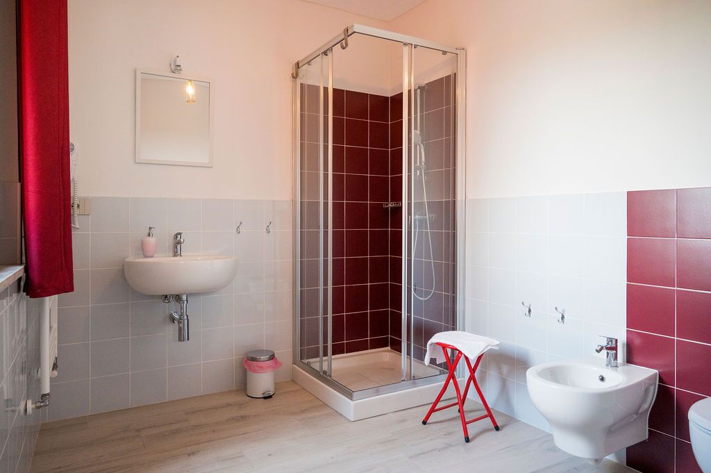 Et moderne badeværelse med et glasafskærmet brusebad, en hvid vask, et toiletbadekar og et rødt håndklædestativ.