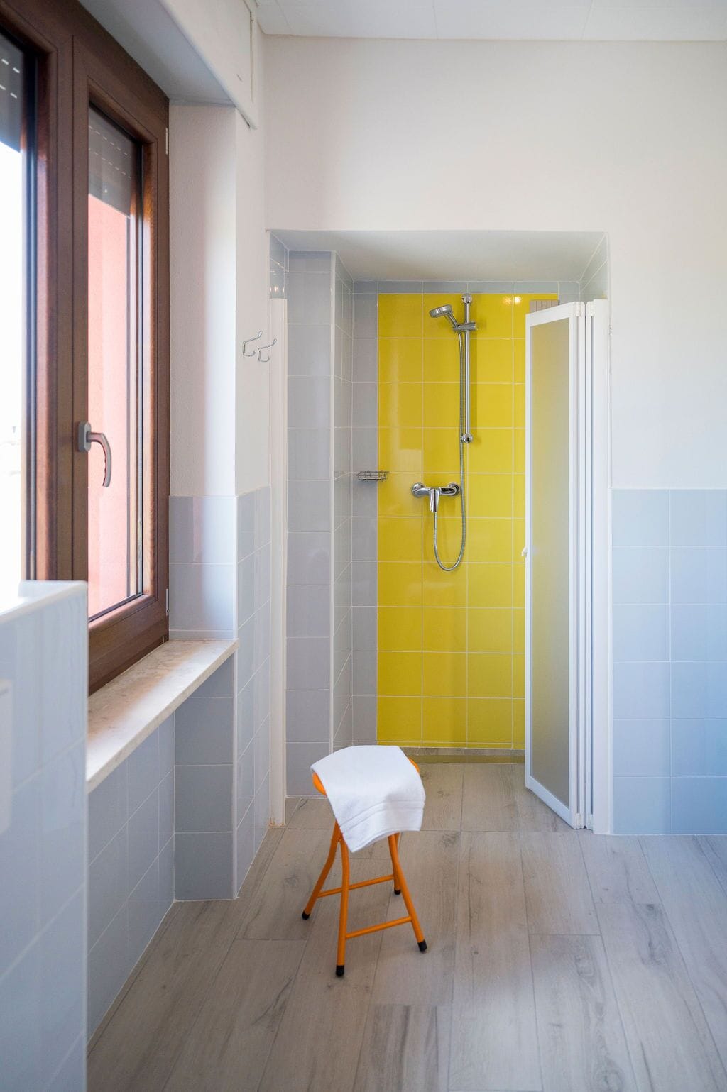 A bathroom with a yellow shower wall, a white sink, and a wooden stool.
