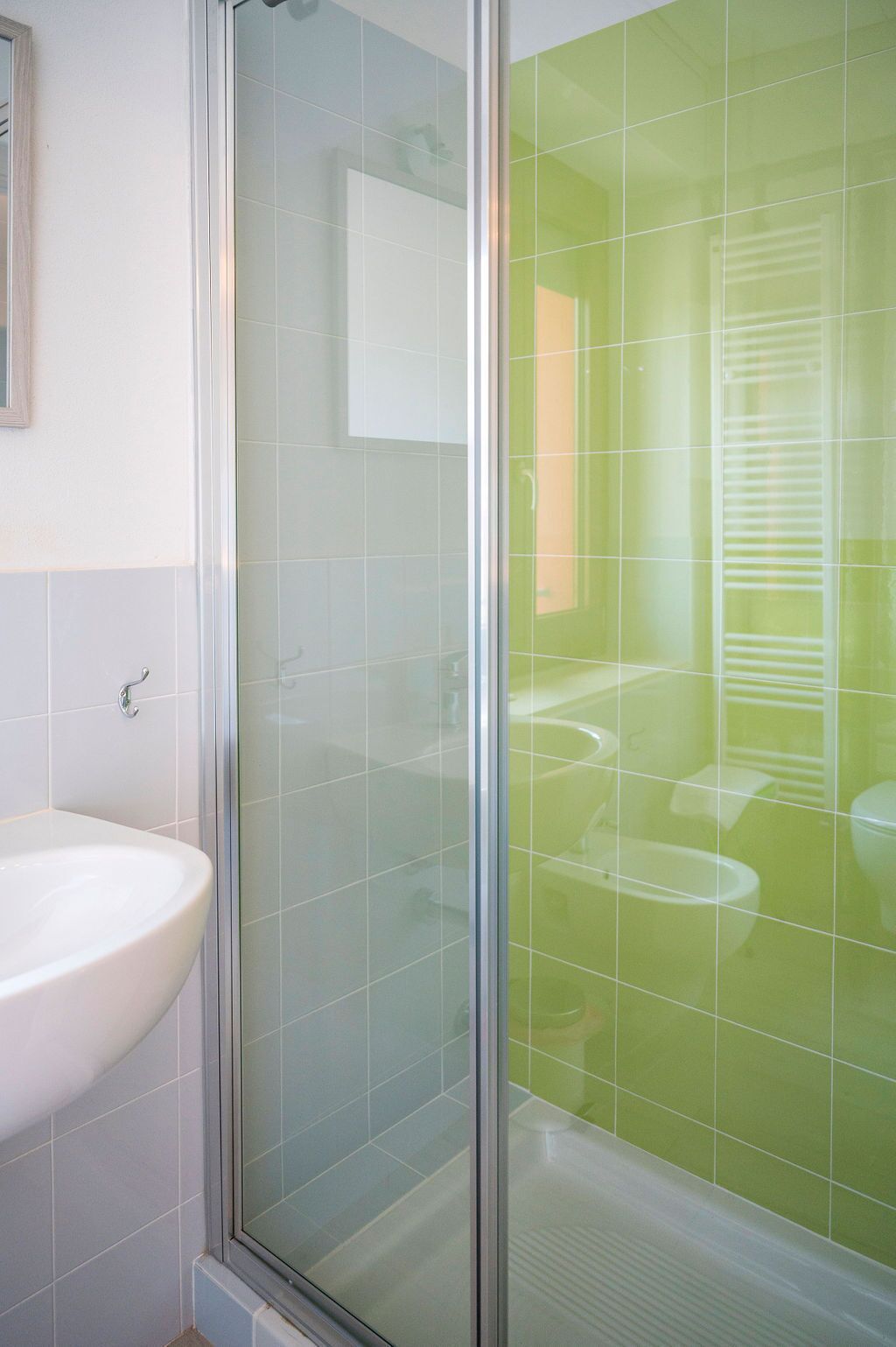Un bagno con box doccia in vetro, lavandino bianco e pareti rivestite di piastrelle verdi.