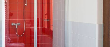 Een badkamer met een douchecabine van glas, een wit toilet en een rode kruk met een witte handdoek.
